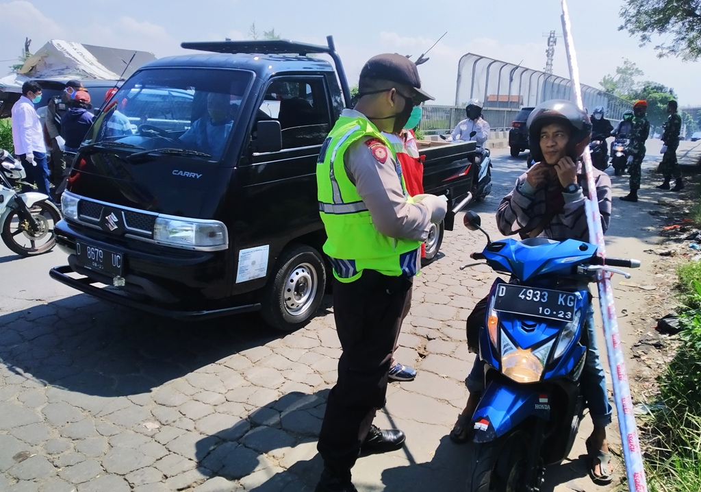 Seorang pengendara sepeda motor yang tidak mengenakan masker diberhentikan oleh seorang anggota polisi di perbtasan Jalan Sadang (Kabupaten Bandung)-Jalan Cibolerang (Kota Bandung), pada hari pertama PSBB Bandung Raya, Jawa Barat, Selasa (22/4/2020). (Foto: Muhammad Zein/dara.co.id)